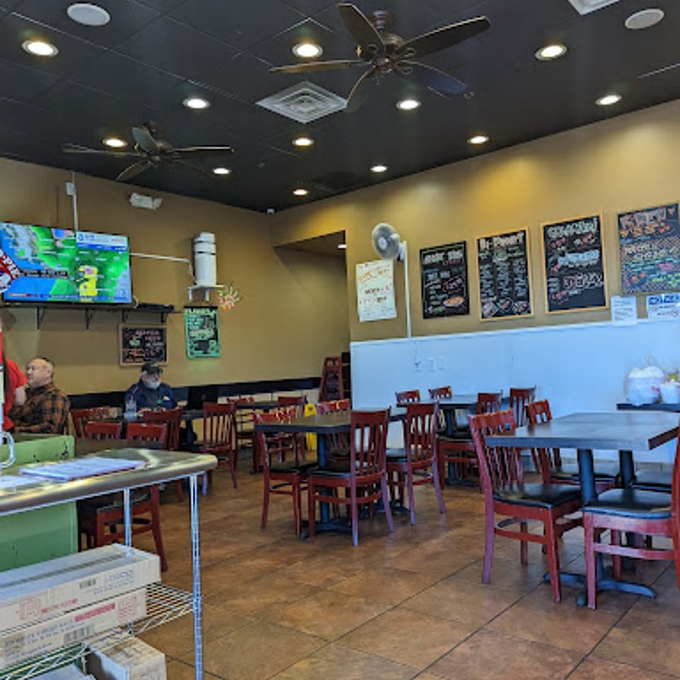 Interior of Yoshi Japanese Cuisine, showing dining tables with red chairs, a TV, and menu boards.