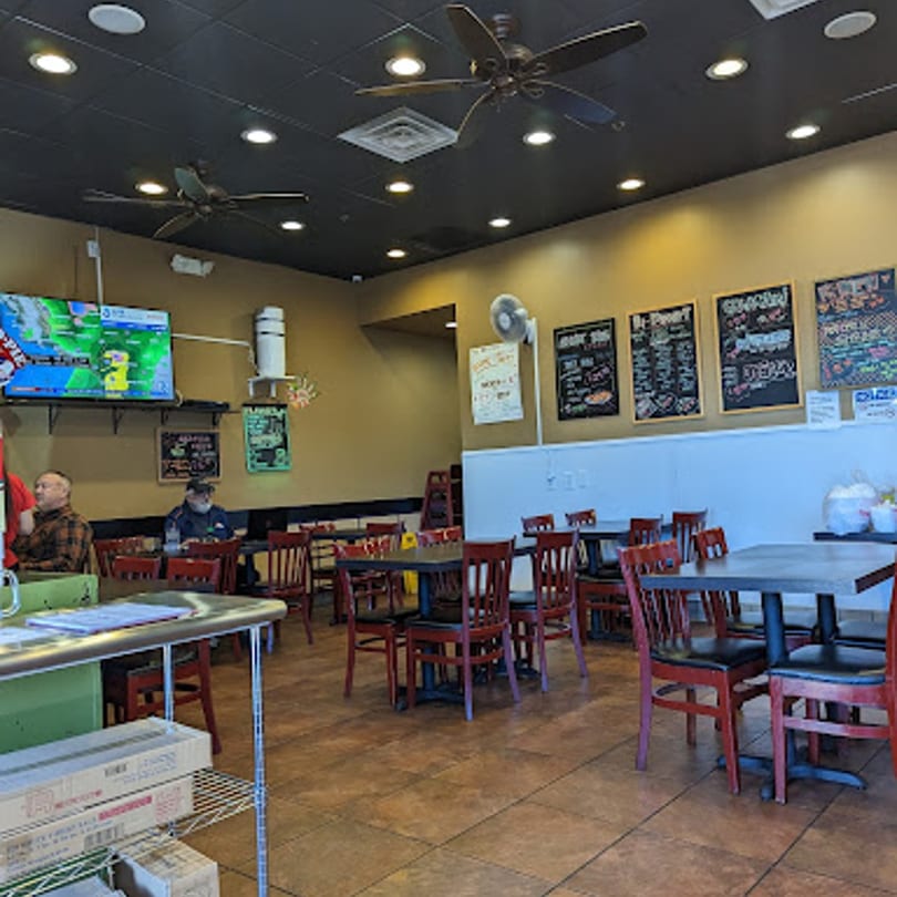 Interior of Yoshi Japanese Cuisine, showing dining tables with red chairs, a TV, and menu boards.