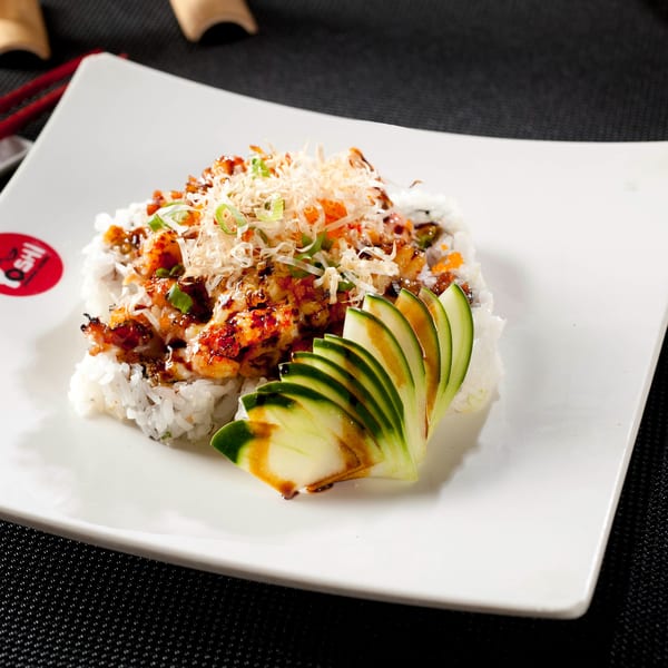 Yoshi Japanese Cuisine's sushi roll topped with sauce, scallions, and bonito flakes, with cucumber slices.