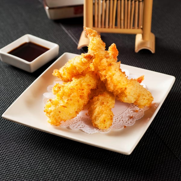 Golden tempura shrimp on a white rectangular plate with a side of soy sauce.