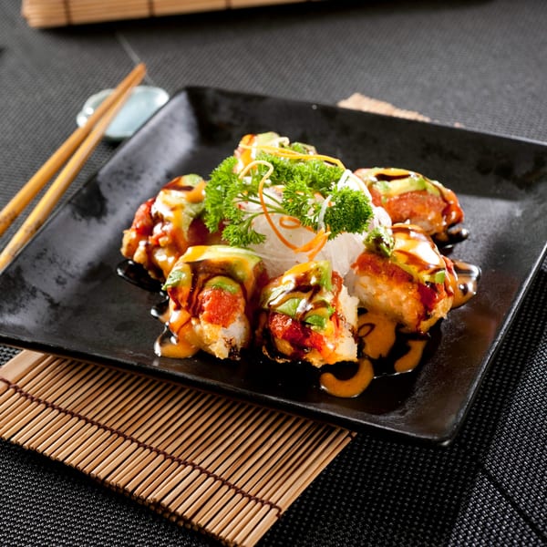 Yoshi Japanese Cuisine's fried sushi rolls with avocado, sauce, and garnish on a black plate with chopsticks.