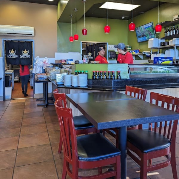 Interior of Yoshi Japanese Cuisine, with red chairs, dark tables, and a sushi bar with staff.